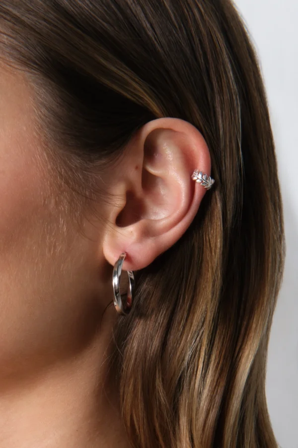 nausznica gałązka i skręcone kolczyki koła srebrne zbliżenie na ucho z nausznicą w kształcie gałązki i kolczykami skręconymi kołami